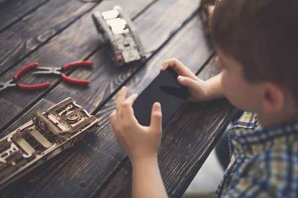 Rapaz progressivo sentado à mesa e segurando o dispositivo moderno em duas mãos — Fotografia de Stock