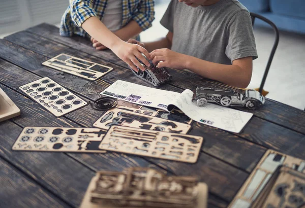 Pedaços de construtor colocados na mesa e dois meninos criando modelos — Fotografia de Stock