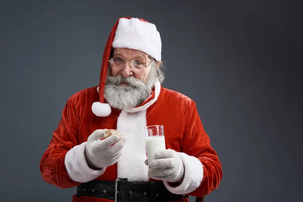 Santa Claus s perníkem a mléko pózuje na šedém pozadí — Stock fotografie