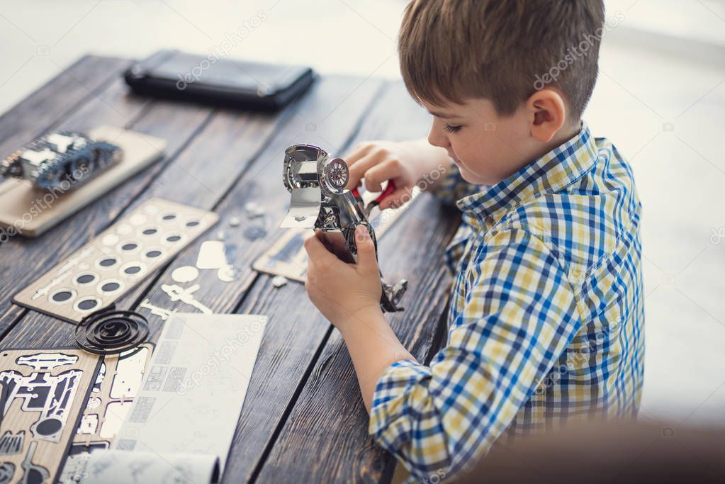 Concentrated boy sitting alone and making metal car model