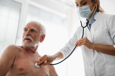 Kadın doktor stetoskop ile koruyucu maske muayene hastada