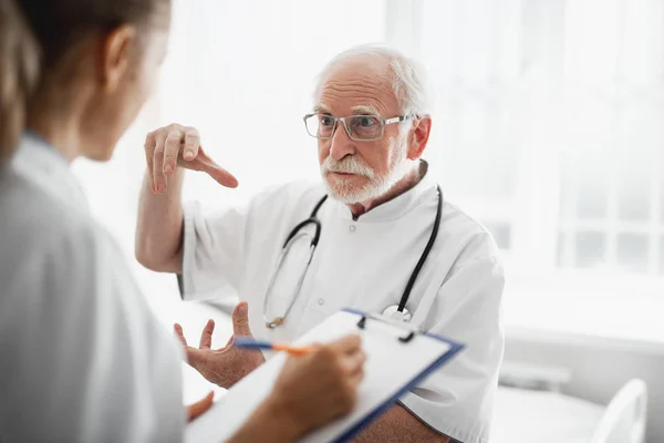 Médico velho explicando algo à enfermeira usando gestos de mão — Fotografia de Stock