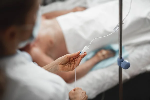 Arzt überprüft intravenösen Tropf während der Ruhe des Patienten — Stockfoto