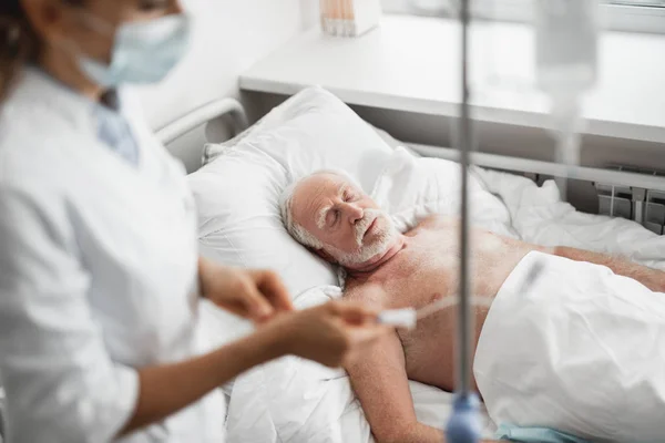 Alter Mann schläft, während Arzt intravenösen Tropf überprüft — Stockfoto