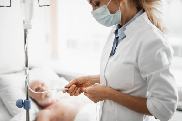 Arzt mit Schutzmaske überprüft intravenösen Tropf im Krankenhauszimmer — Stockfoto