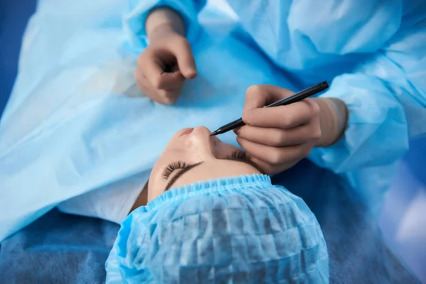 Ретельний лікар тримає чорний маркер і малює лінії на обличчі пацієнта — стокове фото