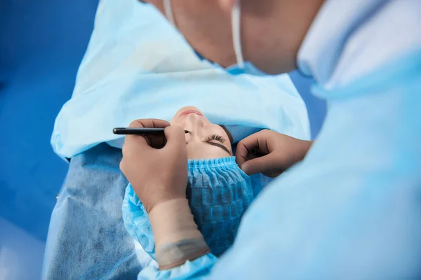 Вид зверху лікаря малює лінії на обличчі молодого пацієнта — стокове фото