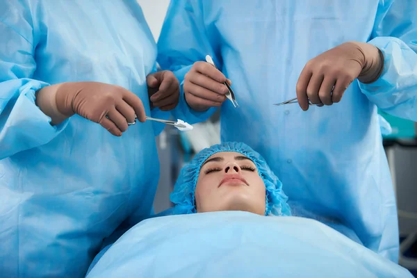 Cirurgiões profissionais segurando instrumentos médicos e em pé perto dos pacientes — Fotografia de Stock