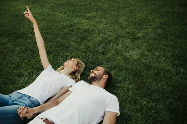 Jovem casal alegre tendo descanso na grama verde — Fotografia de Stock