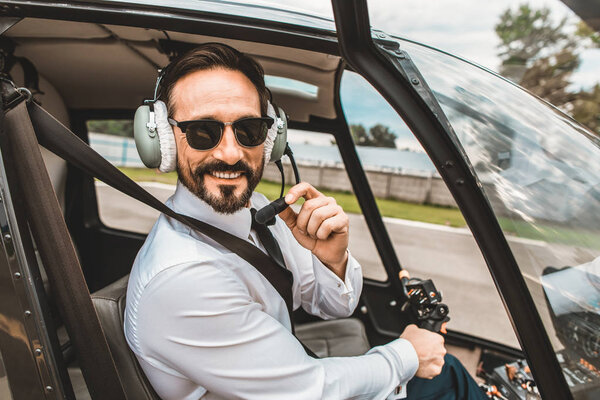 Confident pilot smiling and touching the microphone of headphones