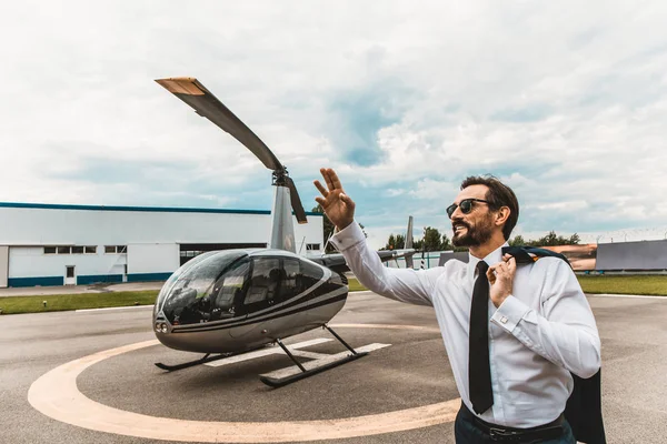Alegre hombre levantando una mano mientras está de pie cerca del helicóptero — Foto de Stock