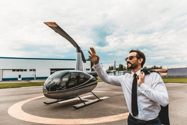 Cheerful man putting one hand up while standing near the helicopter