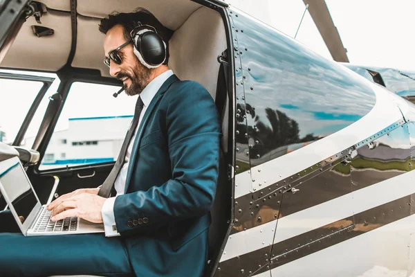 Hombre feliz sentado en la cabina del helicóptero y usando el portátil — Foto de Stock