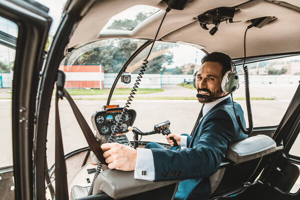 Confident man in elegant suit smiling while being in the helicopter cabin