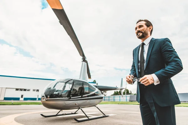 Atractivo hombre de negocios barbudo de pie cerca del helicóptero y sonriendo — Foto de Stock