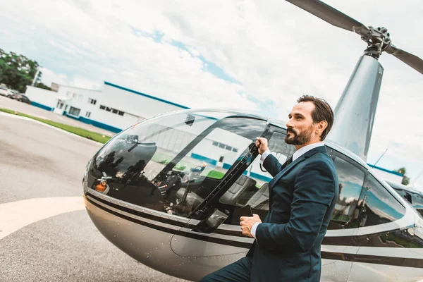 Elegante hombre de negocios tocando la puerta de su helicóptero y buscando confiado — Foto de Stock