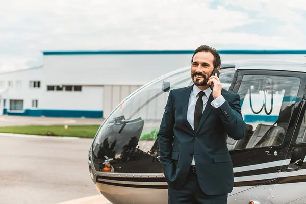 Hombre barbudo con traje oscuro hablando por teléfono cerca del helicóptero — Foto de Stock