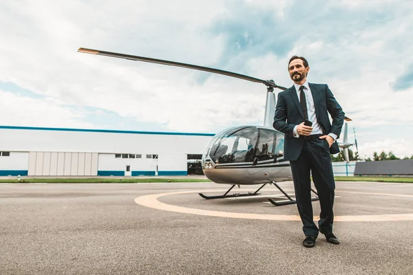 Hombre de negocios confiado sonriendo mientras está de pie cerca del helicóptero — Foto de Stock