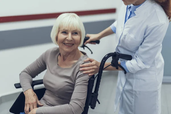 La practicante femenina está impulsando a la feliz mujer discapacitada en la clínica — Foto de Stock