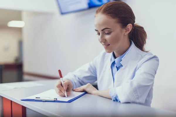 Enfermera positiva está escribiendo en recepción en el hospital —  Fotos de Stock