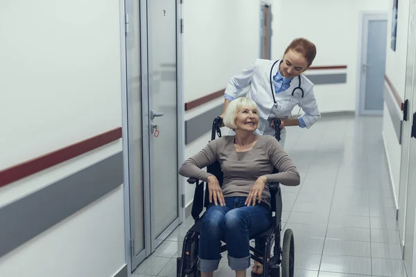 Feliz doctor está empujando silla de ruedas con paciente —  Fotos de Stock