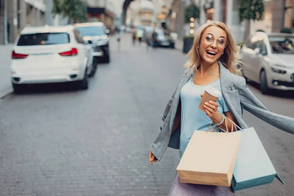 Mujer alegre con bebida caliente caminando por la calle — Foto de Stock