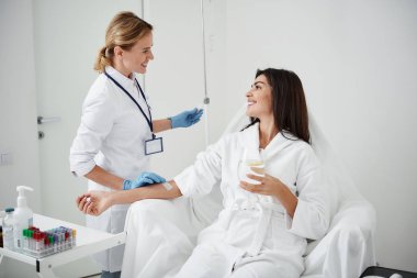 İntravenöz damla gülümseme ile genç kadına bakarken düzenleyen doktor