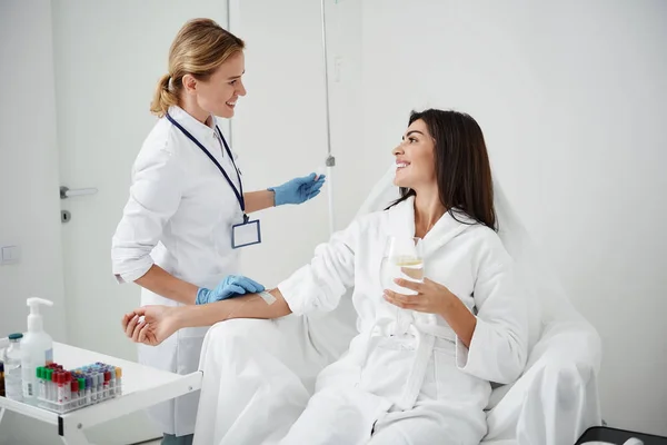 Doctor regulating intravenous drip while looking at young lady with smile — Stock Photo, Image