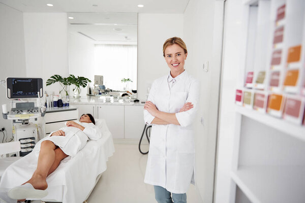 Очаровательный косметолог позирует со скрещенными руками, пока юная леди отдыхает
