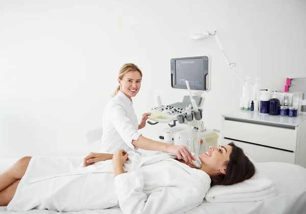 Médico sonriente haciendo prueba de ultrasonido tiroideo para mujer joven — Foto de Stock