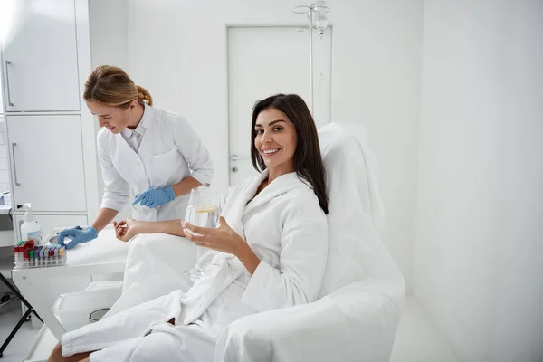 Young lady with drink receiving intravenous treatment at wellness center — Stock Photo, Image