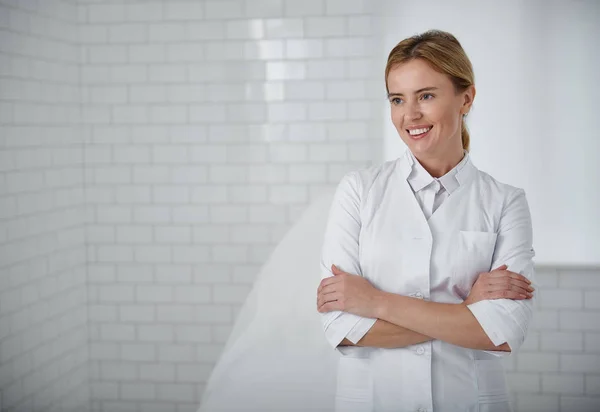 Charming beautician crossing arms while standing at her cabinet — Stock Photo, Image