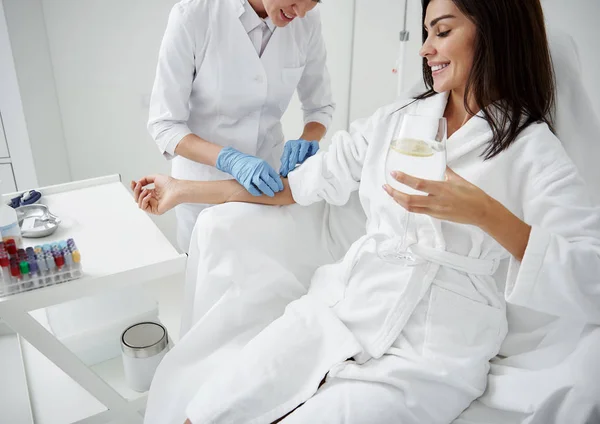 Arzt intravenös Tropfen auf die Hand der Dame, während sie Wasser trinkt — Stockfoto