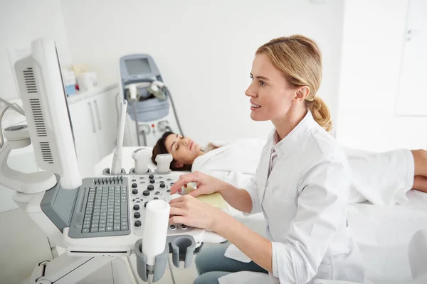 Médico comprobando los resultados del examen médico mientras la joven dama descansa — Foto de Stock