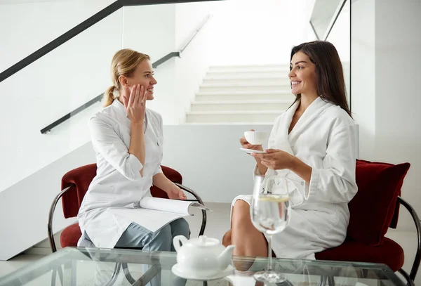 Jonge dame bespreken huid zorg behandeling met schoonheidsspecialiste onder het genot van thee — Stockfoto