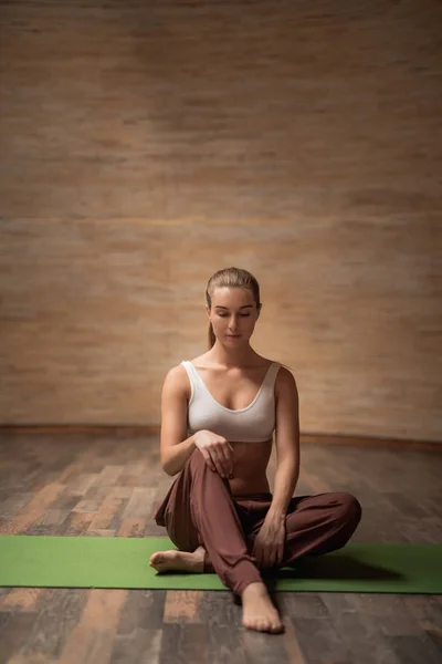 Yoga mat oturma ve genç bir diz bükme genç bayanın tam uzunlukta — Stok fotoğraf