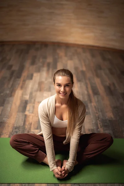 Comprimento total de senhora alegre sentado no tapete de ioga e olhando feliz — Fotografia de Stock