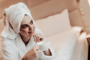 Genç kadın yatakta yatarken çay ile bornoz