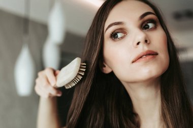 Focused woman combing long dark hair indoor clipart
