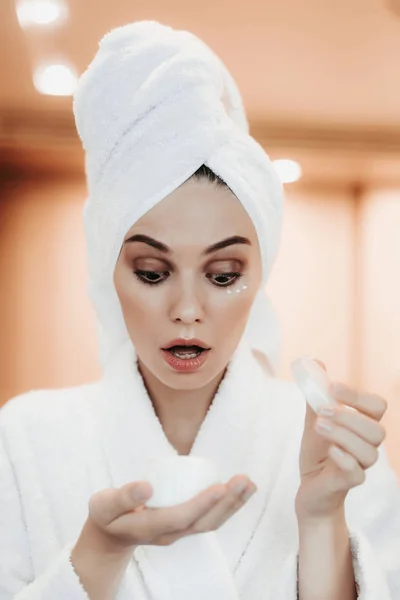 Mujer joven sosteniendo crema facial después de la ducha —  Fotos de Stock