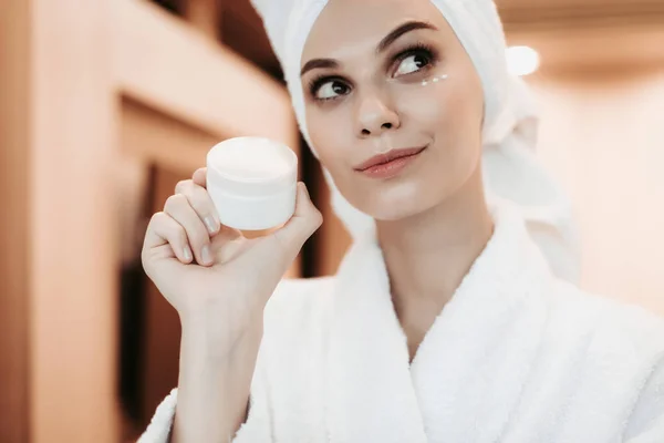 Jovem mulher aplicando creme no rosto após o chuveiro — Fotografia de Stock