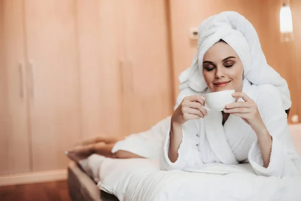 Jonge vrouw in badjas liggend op bed met thee — Stockfoto