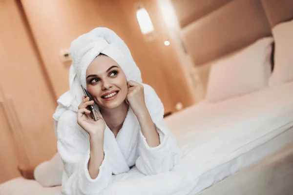 Молодая женщина в халате разговаривает по телефону на кровати — стоковое фото
