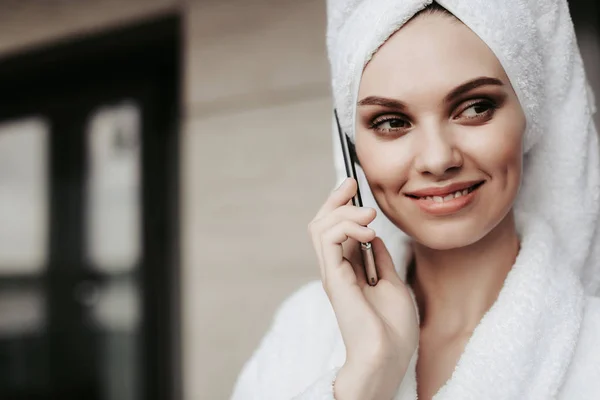 Young woman in bathrobe talking by phone — Stock Photo, Image