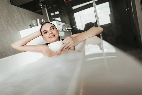 Sonriente dama tomando baño de burbujas con té —  Fotos de Stock