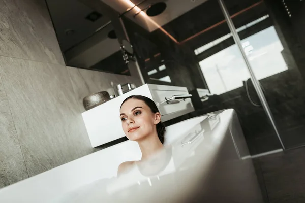 Sorrindo senhora tomando banho de espuma relaxante em casa — Fotografia de Stock