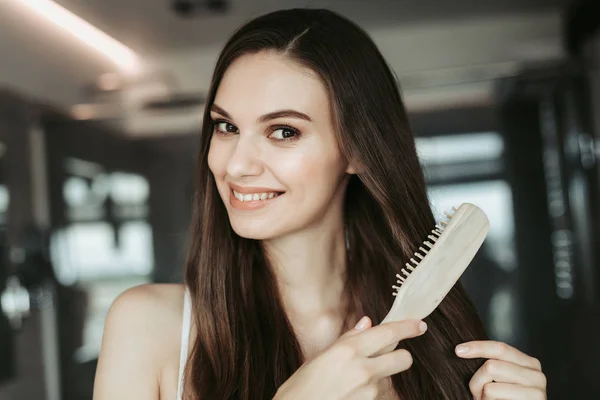 Menina alegre escovando cabelo castanho no apartamento — Fotografia de Stock