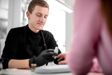 Dikkatli manikürcü. Siyah lateks eldiven giymiş ve müvekkilinin tırnak parlatma gülümseyen profesyonel genç adam