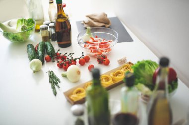 Mutfak masasında taze sebze, bir şişe şarap ve makarna ile