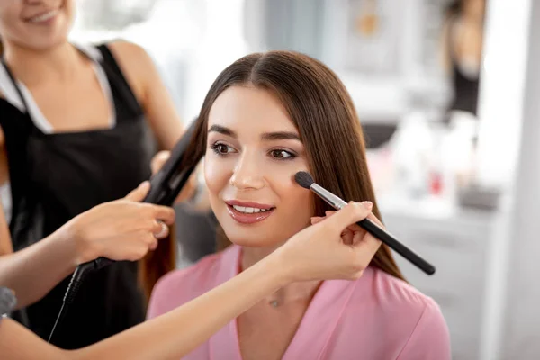 Entspannte Dame lächelt und Kosmetikerin macht Make-up für sie — Stockfoto